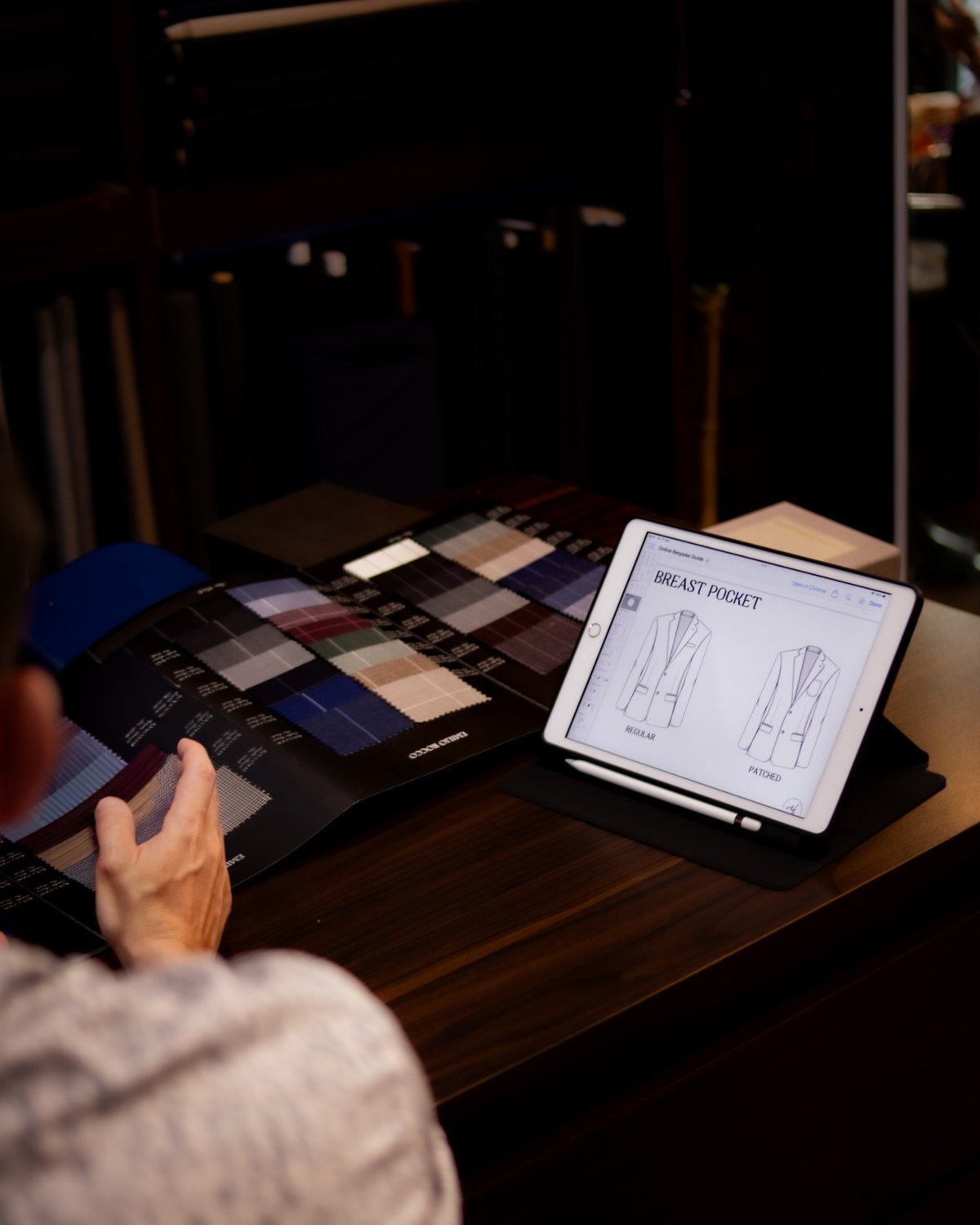 Choosing jacket details on a tablet beside a book of shirting swatches
