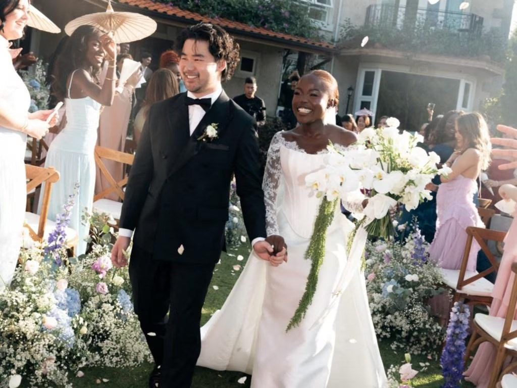 A groom in a black tuxedo and his bride walking down the aisle